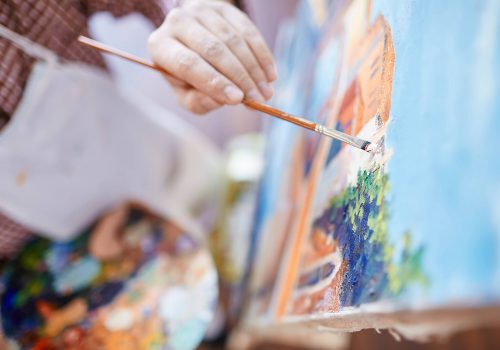 Hand of artist with paintbrush painting on canvas